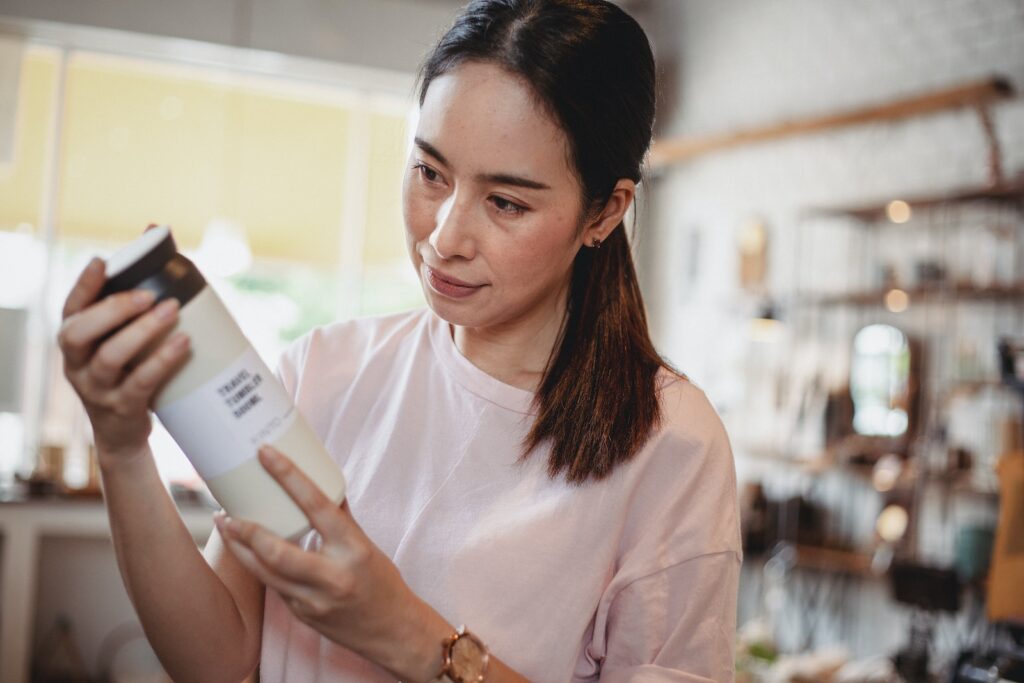 Crop young attentive ethnic shopper reading information on bottle of cosmetic product in store