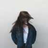 woman wearing blue denim jacket standing near white concrete wall